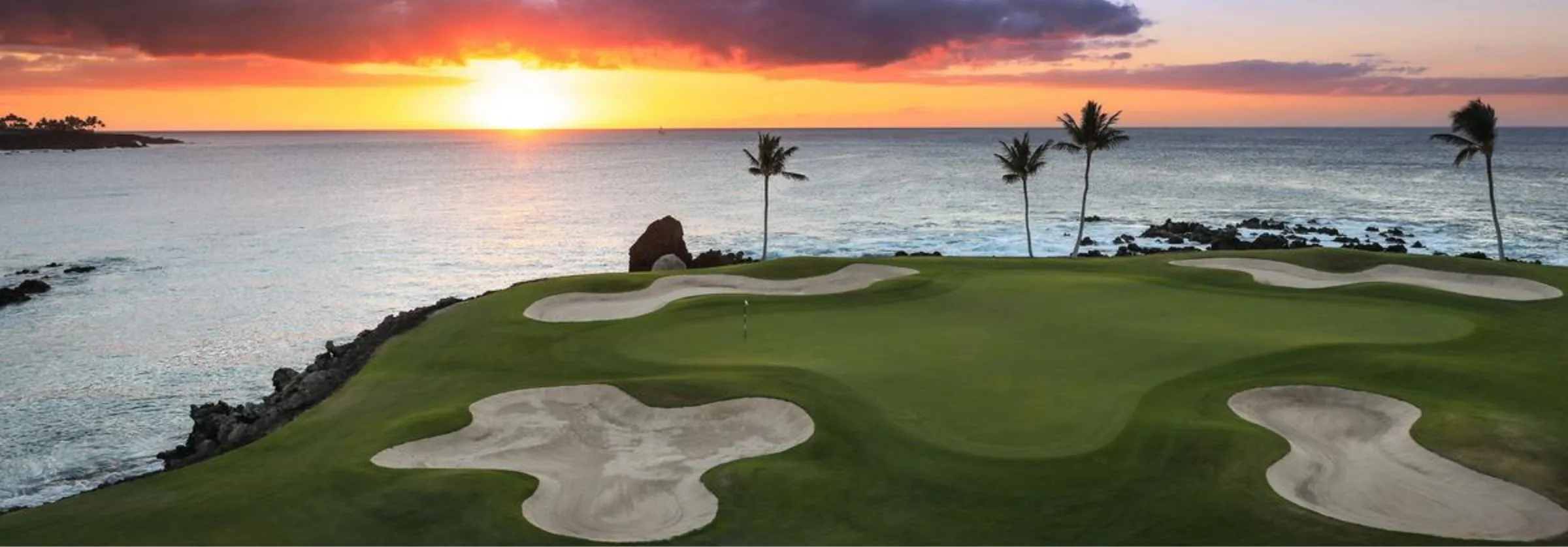 Golf course by ocean at sunset with palm trees.
