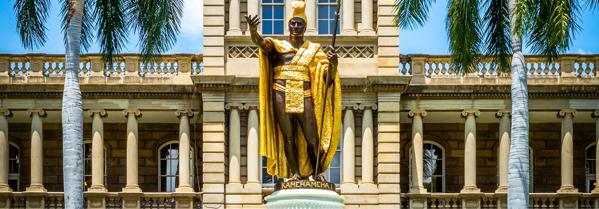 Golden statue of King Kamehameha I in front of a historic government building.