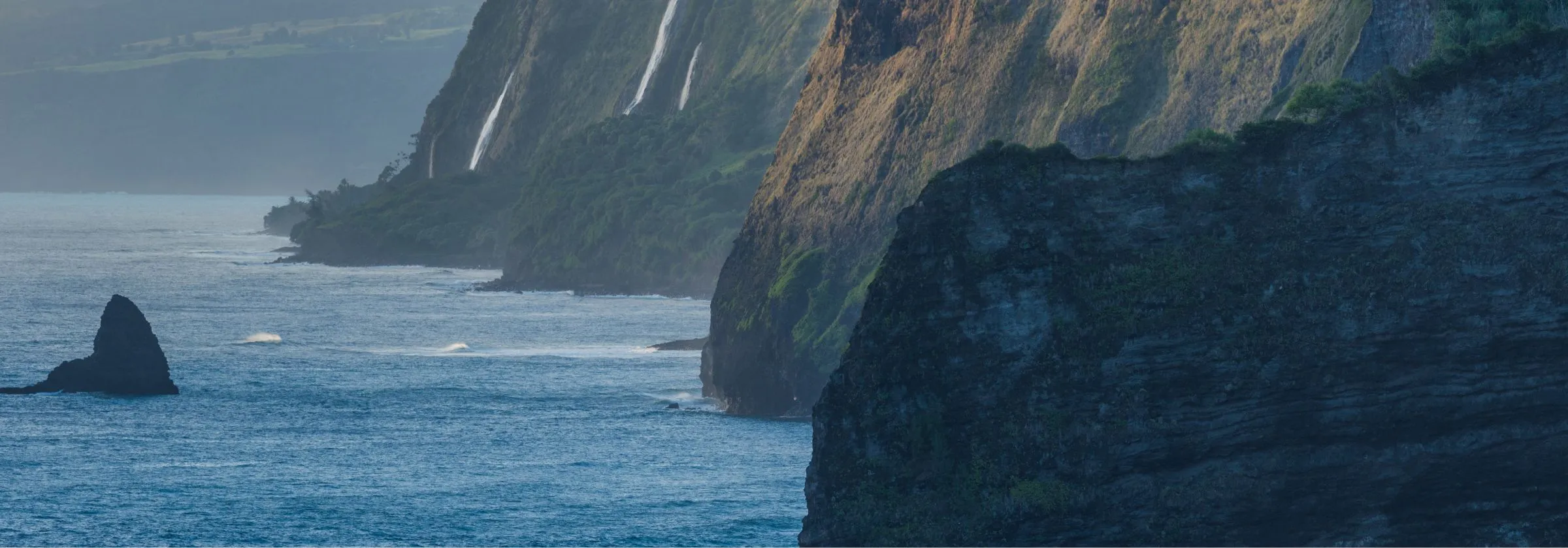 Cliffs with waterfalls overlooking the ocean at sunset.