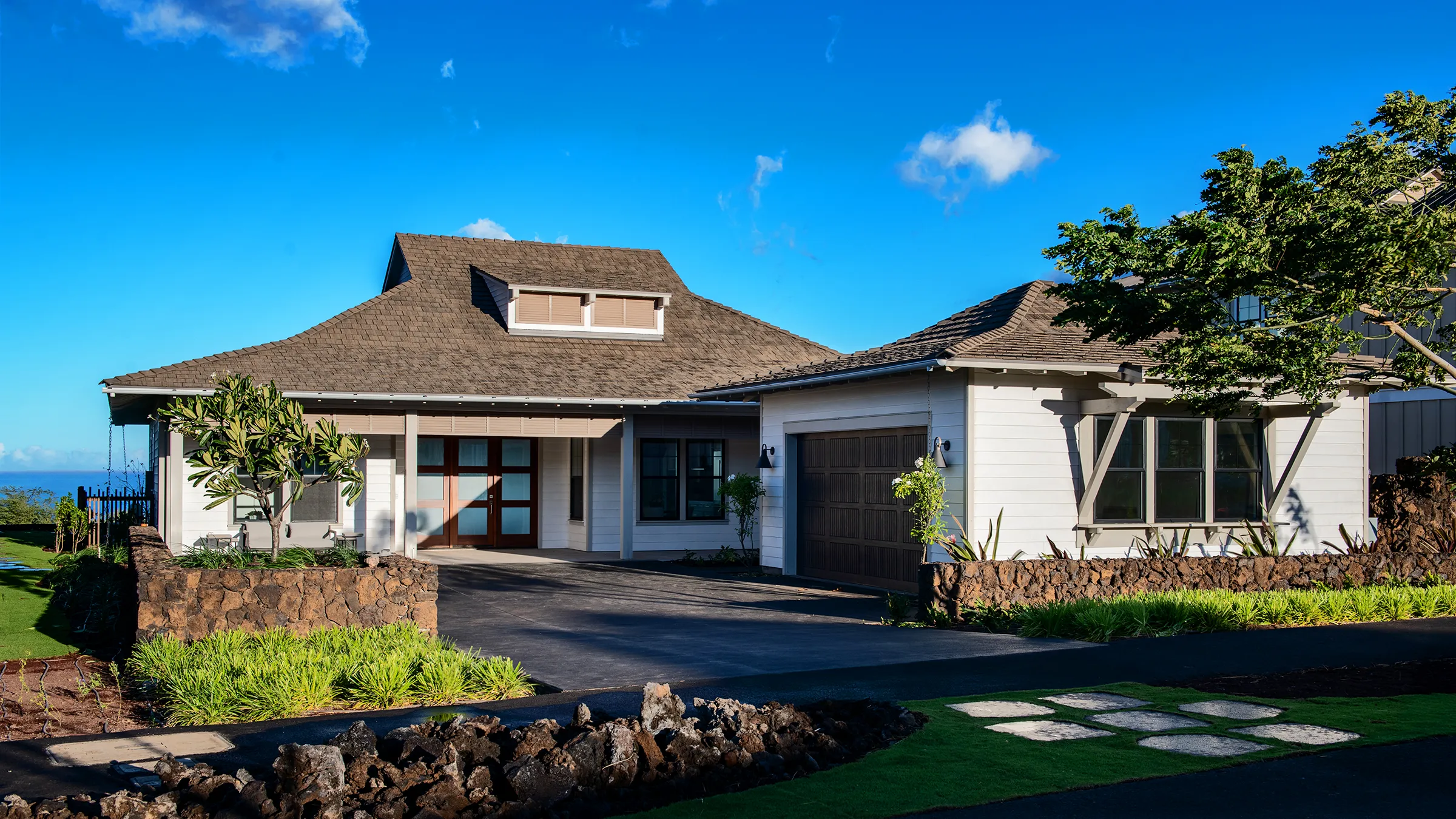 Single-story house with a red roof, surrounded by greenery and a paved driveway.