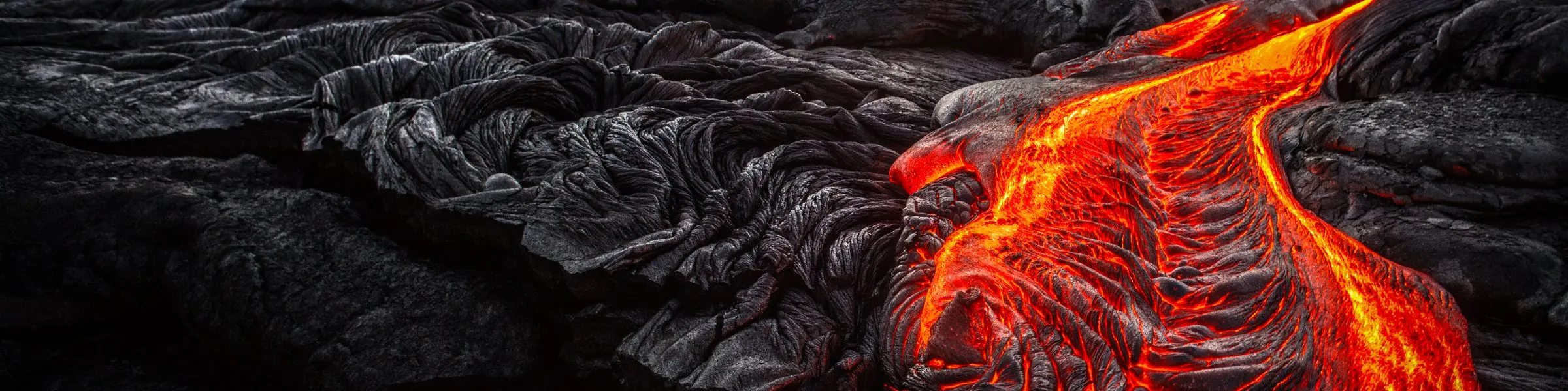 Molten lava flowing over dark, hardened rock surface.
