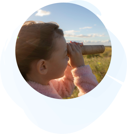 A child in a pink sweater peers through a cardboard tube, standing in a grassy field under the pristine sky of Nānā Kai.