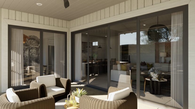 A modern patio with wicker chairs, a small table with a vase, and large sliding glass doors leading to an interior room with wall art and pendant lights.