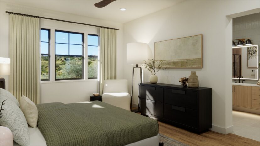 A modern bedroom with a green bedspread, a large window, a dark dresser, and a white armchair. A partially visible bathroom can be seen on the right.